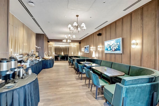 dining area with a notable chandelier, wooden walls, and light hardwood / wood-style flooring