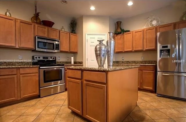 kitchen featuring light tile patterned flooring, dark stone countertops, appliances with stainless steel finishes, and a kitchen island