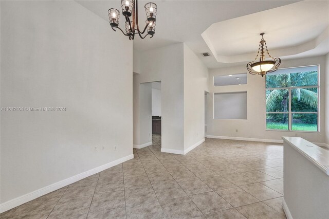 tiled empty room with an inviting chandelier and a tray ceiling