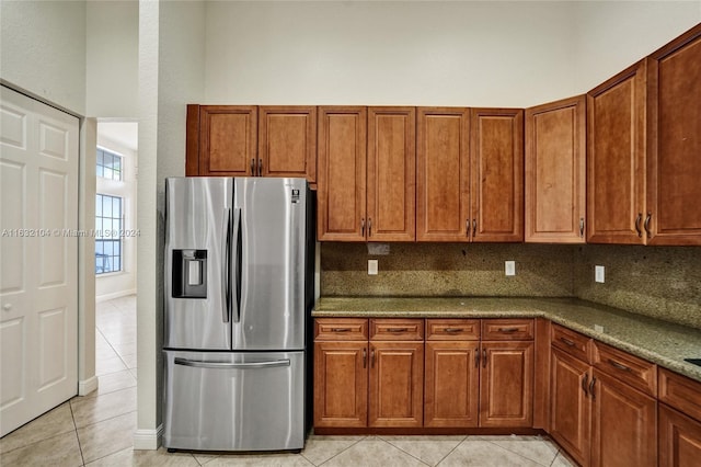 kitchen featuring light tile patterned floors, backsplash, stainless steel fridge, and light stone countertops