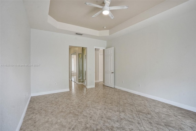 spare room with ceiling fan, a tray ceiling, and light tile patterned floors