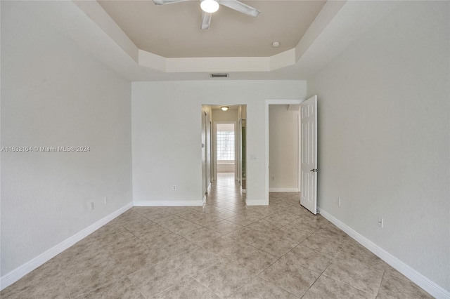 tiled empty room featuring ceiling fan and a tray ceiling