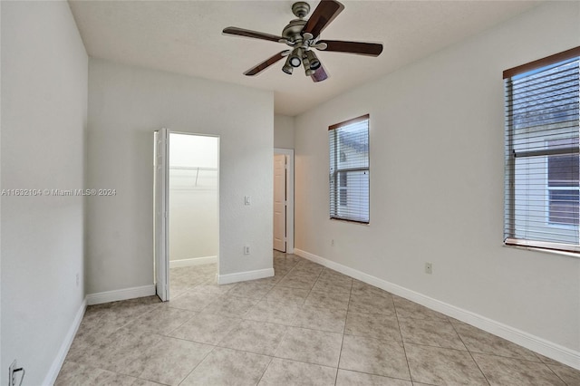 unfurnished bedroom with light tile patterned floors, a spacious closet, a closet, and ceiling fan