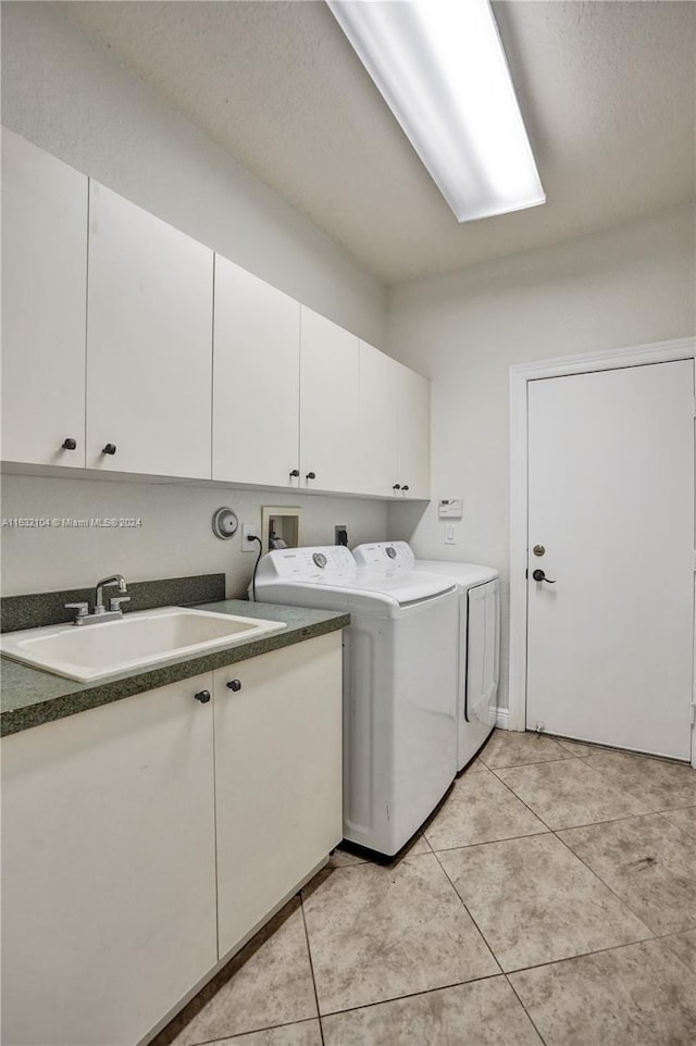 clothes washing area with sink, light tile patterned floors, cabinets, and washing machine and clothes dryer