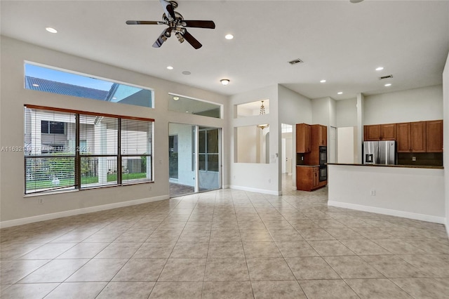 unfurnished living room with ceiling fan, a towering ceiling, a healthy amount of sunlight, and light tile patterned flooring