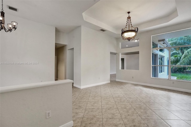 tiled spare room with a raised ceiling and a notable chandelier