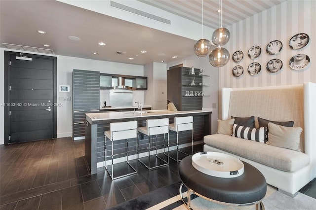 interior space featuring decorative light fixtures, an island with sink, sink, a kitchen bar, and wall chimney exhaust hood