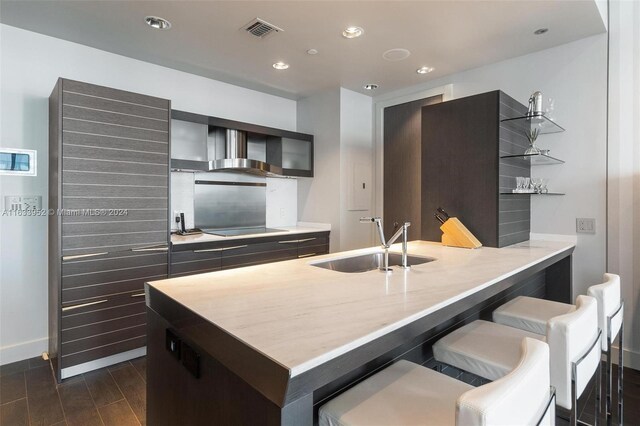 kitchen with a breakfast bar area, black electric cooktop, dark hardwood / wood-style flooring, wall chimney exhaust hood, and sink