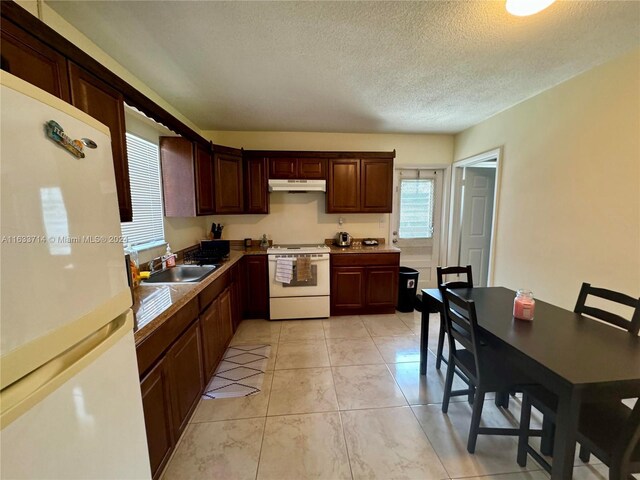 kitchen with white appliances, sink, light tile patterned floors, dark brown cabinetry, and a textured ceiling