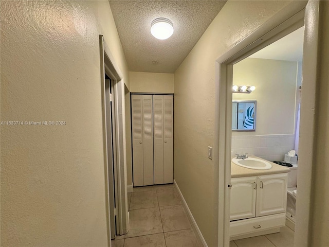 hall with sink, a textured ceiling, and light tile patterned floors