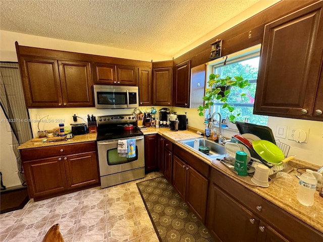 kitchen with light tile patterned flooring, appliances with stainless steel finishes, sink, and a textured ceiling