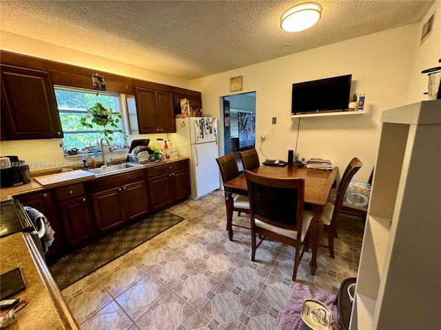 kitchen featuring sink, white fridge, dark brown cabinets, and light tile patterned floors