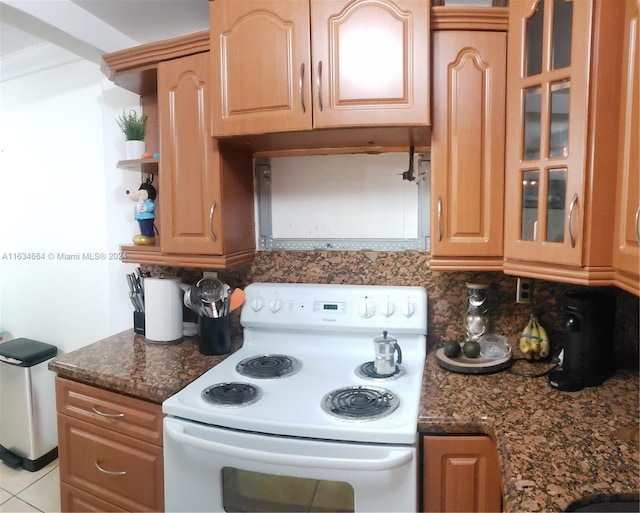 kitchen featuring white electric range oven, backsplash, light tile patterned flooring, and dark stone countertops