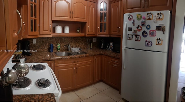 kitchen featuring white appliances, sink, decorative backsplash, dark stone countertops, and light tile patterned flooring