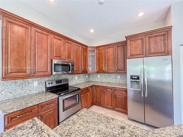 kitchen featuring stainless steel appliances, tasteful backsplash, light tile patterned floors, and a textured ceiling