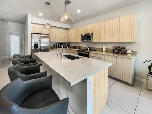 kitchen featuring light brown cabinets, sink, an island with sink, appliances with stainless steel finishes, and decorative light fixtures