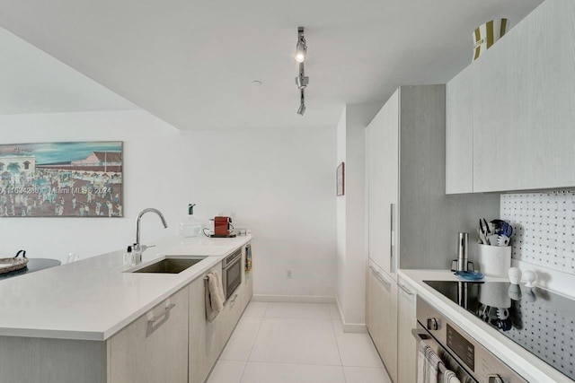 kitchen with rail lighting, stainless steel oven, black electric cooktop, sink, and light tile patterned flooring