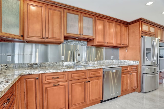 kitchen with stainless steel appliances, sink, light stone countertops, and backsplash