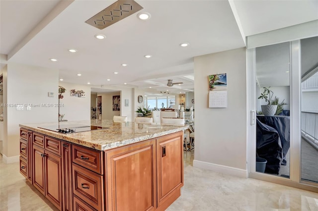 kitchen with black electric stovetop, ceiling fan, light stone counters, and a kitchen island