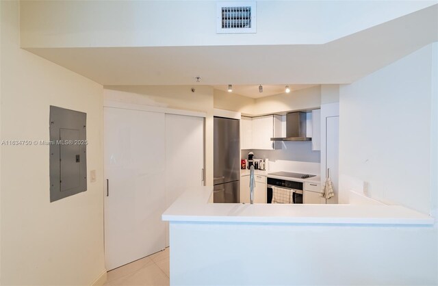 kitchen featuring stainless steel refrigerator, oven, electric panel, kitchen peninsula, and wall chimney range hood