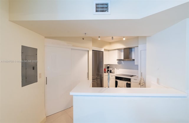 kitchen with stainless steel refrigerator, electric panel, kitchen peninsula, wall oven, and wall chimney range hood