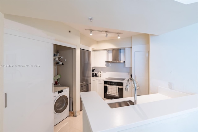 kitchen with wall chimney exhaust hood, washer / dryer, black appliances, kitchen peninsula, and white cabinets