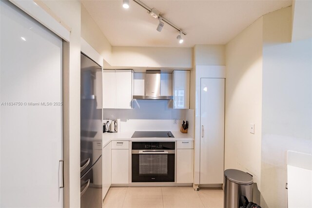 kitchen with wall oven, white cabinets, black electric cooktop, and wall chimney exhaust hood