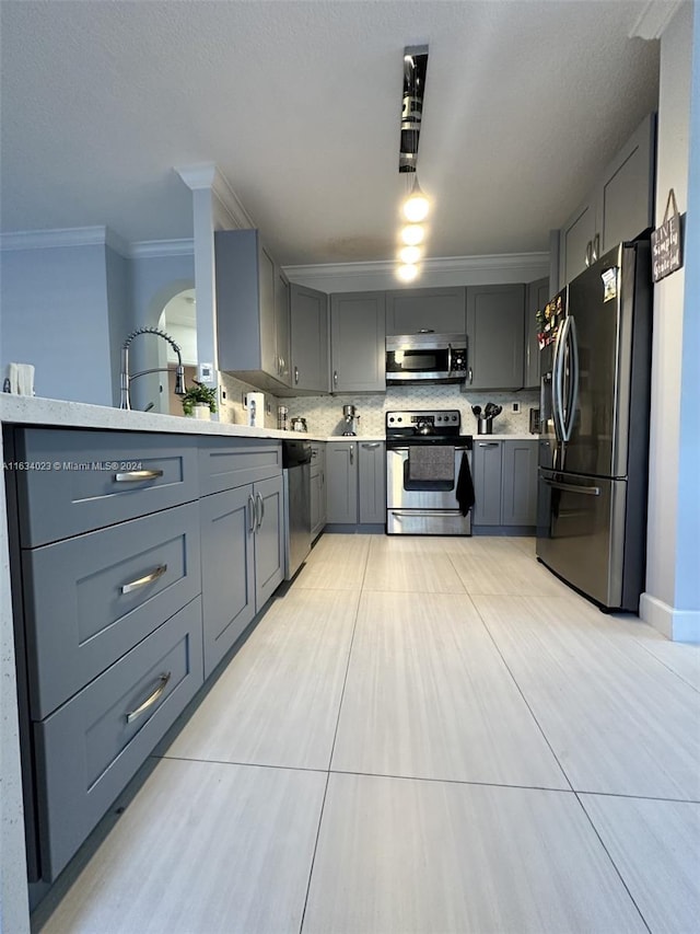 kitchen featuring tasteful backsplash, light tile patterned floors, gray cabinets, stainless steel appliances, and ornamental molding