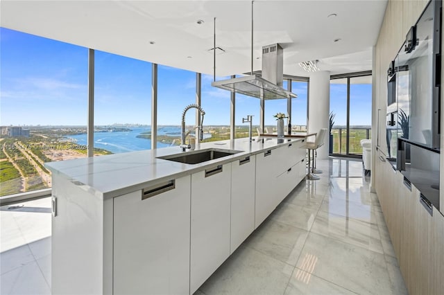 kitchen with white cabinetry, a water view, sink, light stone countertops, and a center island with sink