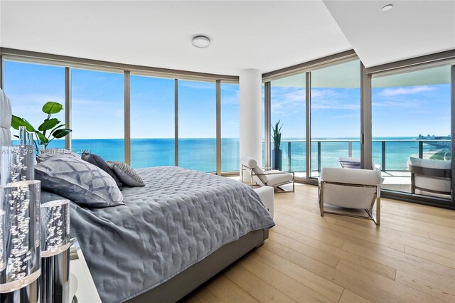 bedroom with a water view, light hardwood / wood-style flooring, and expansive windows