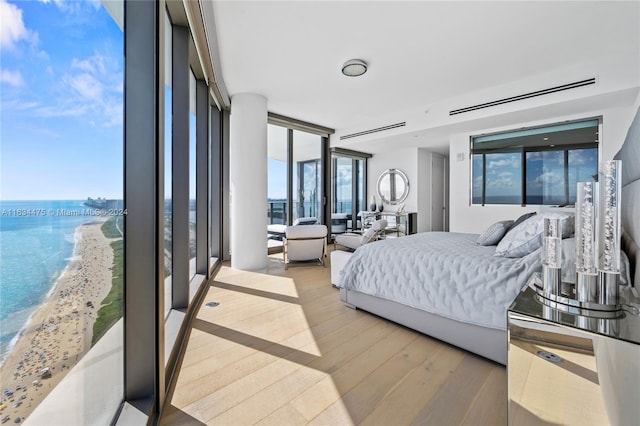 bedroom with a beach view, a water view, light hardwood / wood-style floors, and a wall of windows