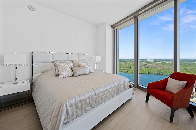 bedroom featuring a water view, expansive windows, and light wood-type flooring