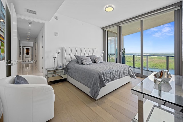 bedroom featuring light wood-type flooring, access to outside, visible vents, and a wall of windows