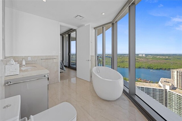 bathroom featuring a water view, toilet, a bathing tub, vanity, and expansive windows