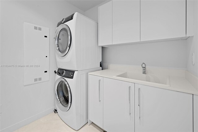 laundry area with stacked washer / drying machine, sink, and cabinets