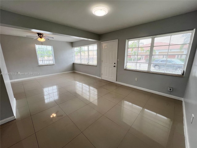 tiled empty room featuring ceiling fan and baseboards