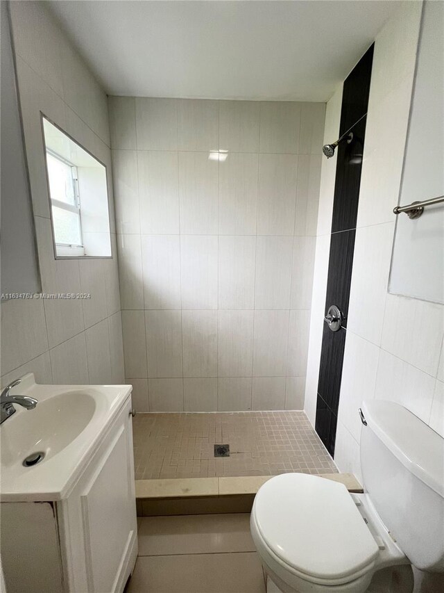 bathroom featuring toilet, tile patterned flooring, vanity, tiled shower, and tile walls