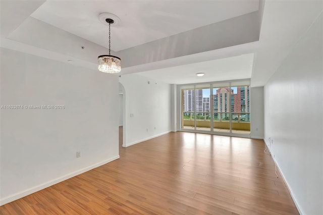 unfurnished room with wood finished floors, arched walkways, a wall of windows, baseboards, and a chandelier