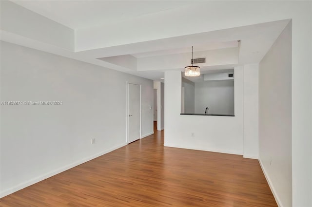 unfurnished room featuring an inviting chandelier, hardwood / wood-style flooring, and a raised ceiling