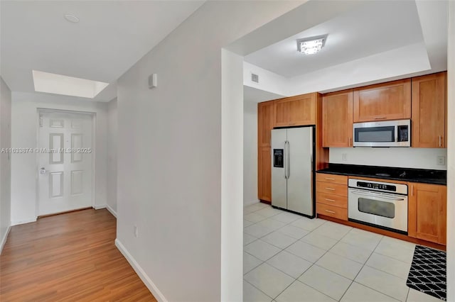 kitchen featuring stainless steel appliances, dark countertops, brown cabinetry, baseboards, and light wood finished floors