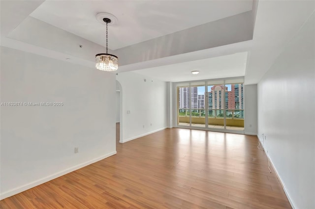 unfurnished room featuring baseboards, wood finished floors, and arched walkways