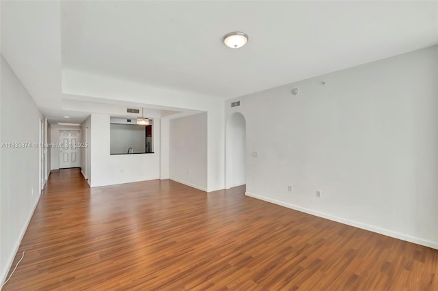 unfurnished living room featuring wood finished floors, arched walkways, and baseboards