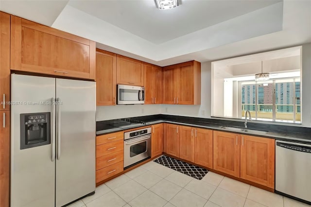 kitchen with stainless steel appliances, pendant lighting, light tile patterned floors, sink, and a tray ceiling