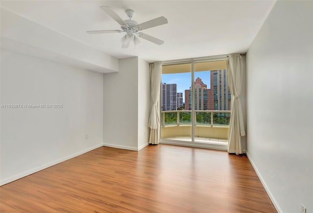 unfurnished room with ceiling fan, baseboards, a city view, and wood finished floors