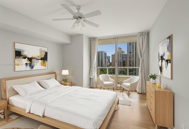 bedroom with light wood finished floors, ceiling fan, and a view of city