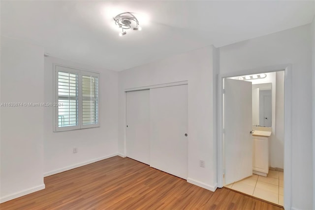 unfurnished bedroom with a closet, connected bathroom, and light hardwood / wood-style floors