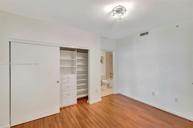 unfurnished bedroom featuring visible vents, light wood finished floors, baseboards, a closet, and connected bathroom