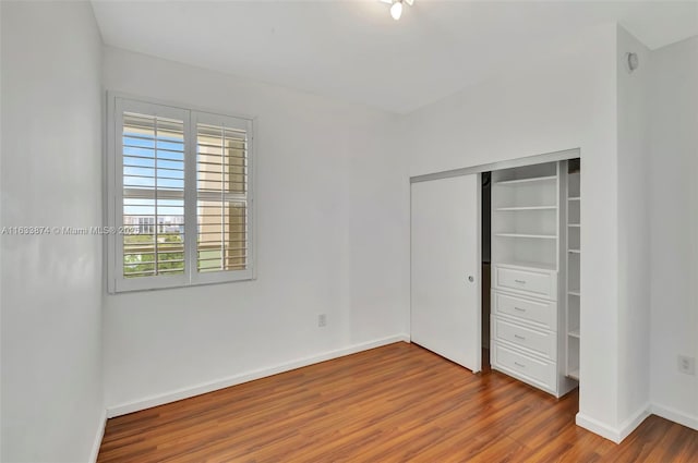 unfurnished bedroom with wood finished floors, baseboards, and a closet