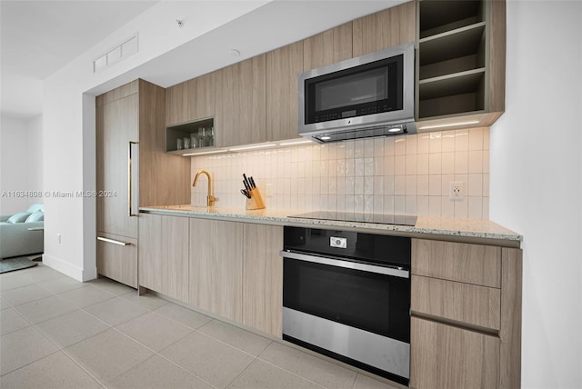 kitchen with stainless steel appliances, light stone counters, decorative backsplash, light tile patterned flooring, and light brown cabinetry