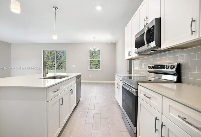 kitchen featuring tasteful backsplash, white cabinets, a kitchen island with sink, appliances with stainless steel finishes, and sink